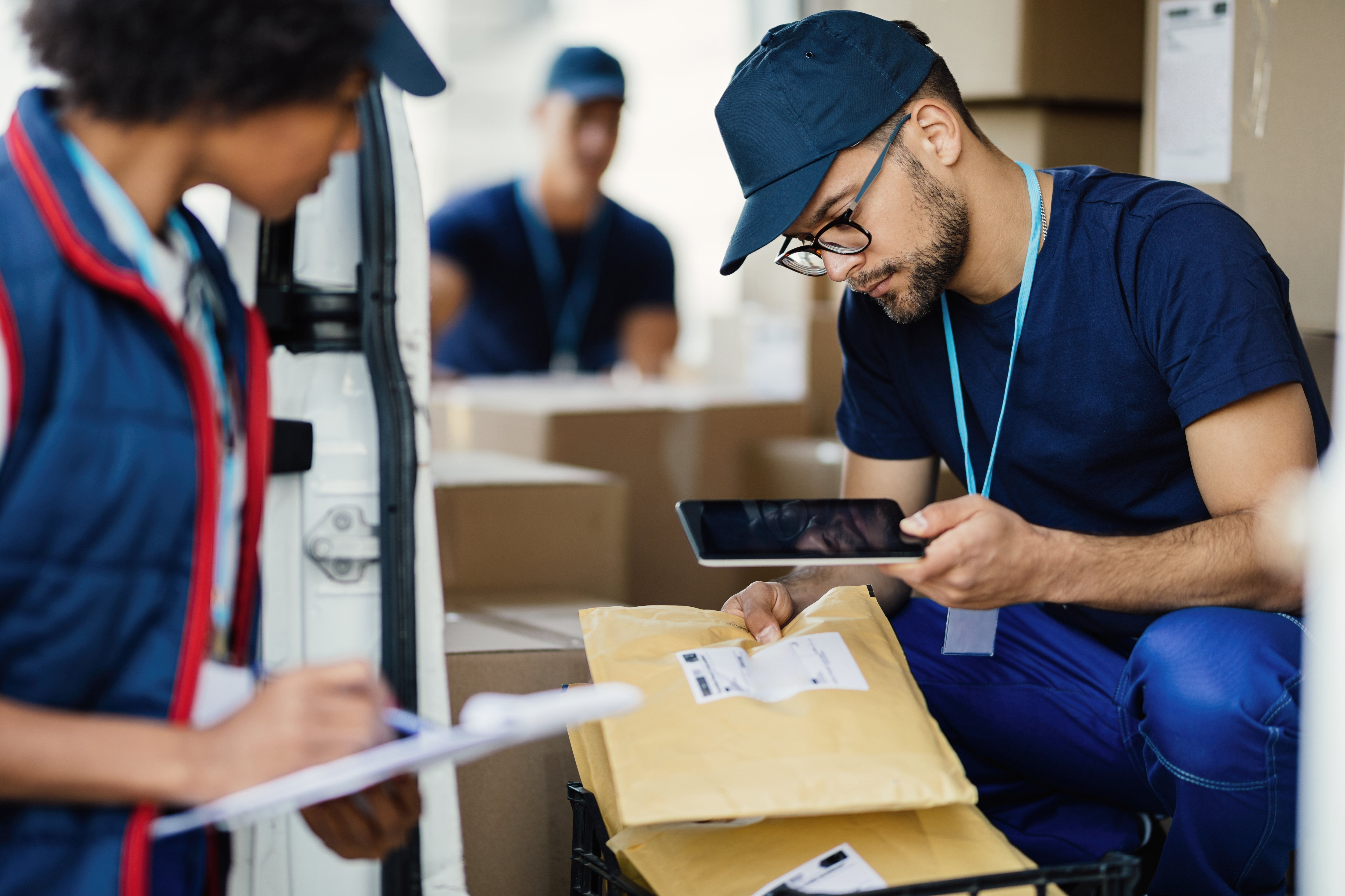 repartidor-joven-que-usa-una-tableta-digital-para-escanear-el-codigo-de-barras-en-la-etiqueta-del-paquete-mientras-se-prepara-para-el-envio-con-su-companero-de-trabajo
